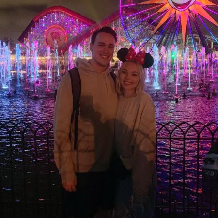 Taylor Hickson and David Nadeau are posing for a picture with an theme park ride in the background.